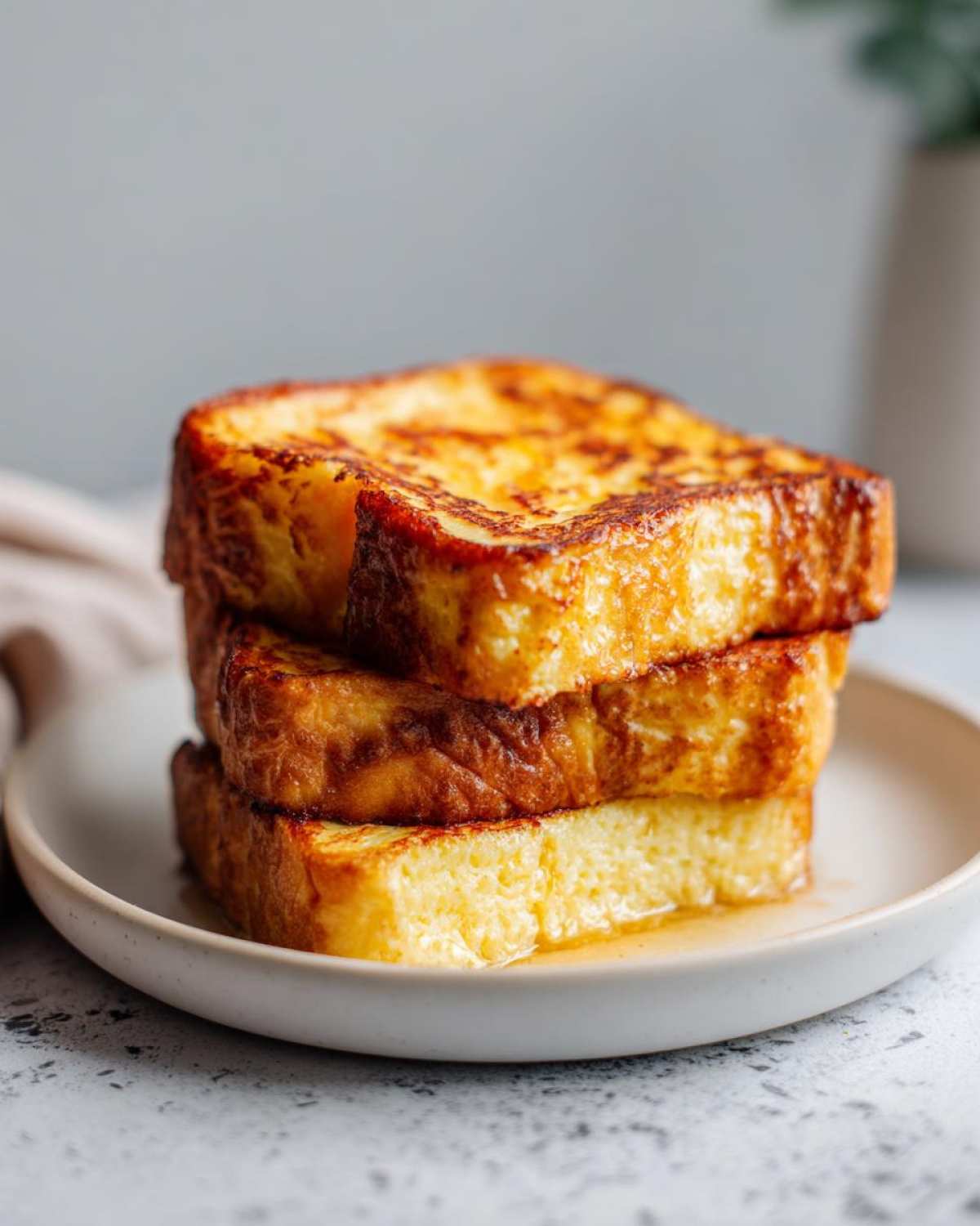 A stack of three thick slices of golden brown easy french toast drizzled with syrup on a light plate.