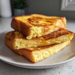 Three thick slices of golden brown easy french toast stacked on a plate, drizzled with syrup.