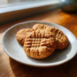 Three golden brown Easy Peanut Butter Cookies with classic crosshatch fork marks on a light ceramic plate.