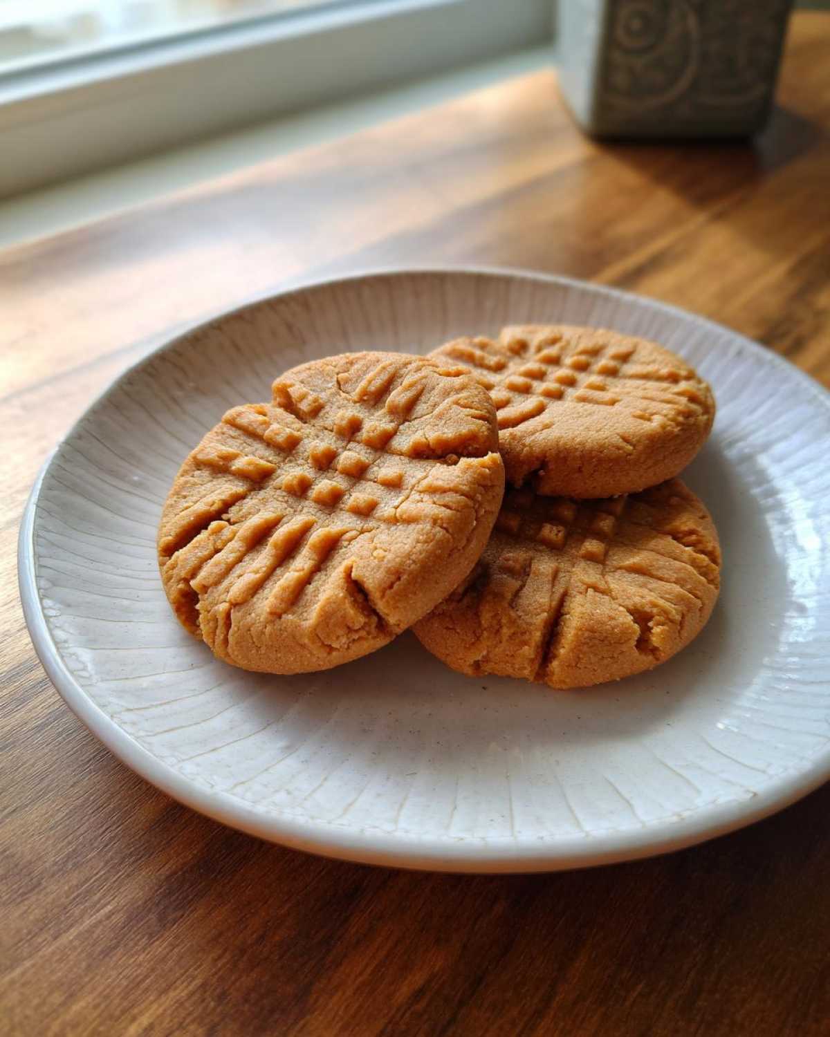 Three classic Easy Peanut Butter Cookies with fork marks displayed on a white, textured plate.
