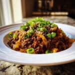 A close-up of a serving of savory Egg Roll in a Bowl, featuring ground meat and cabbage, topped with sliced green onions and sesame seeds.