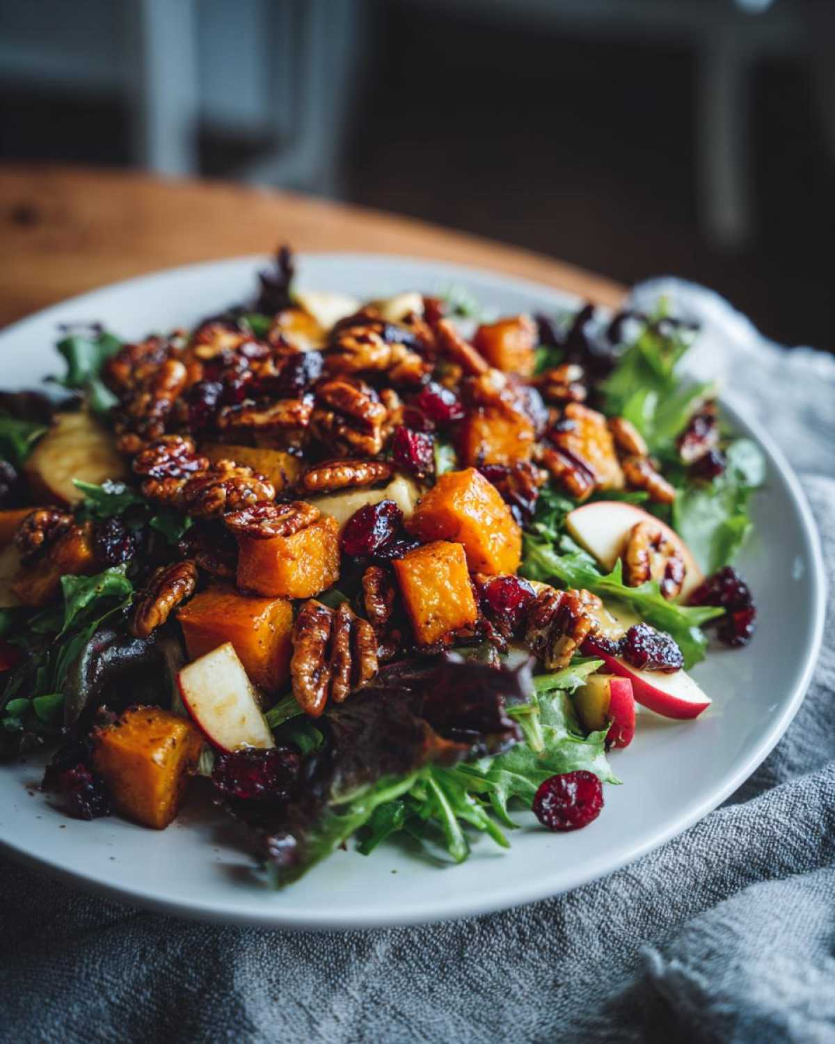 A close-up of an amazing fall harvest salad featuring roasted butternut squash, candied pecans, dried cranberries, and apple slices on mixed greens.