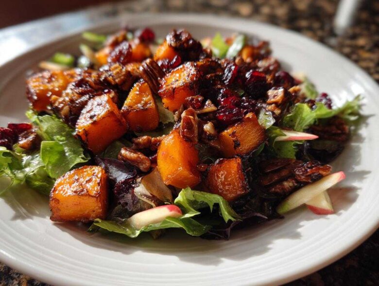Close-up of a vibrant fall harvest salad featuring roasted butternut squash, pecans, and dried cranberries over mixed greens.