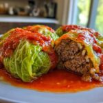 Three delicious cabbage rolls smothered in rich tomato sauce, one cut open showing the ground meat and rice filling.