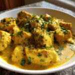 Close-up of tender chicken pieces coated in a rich, yellow coconut sauce, garnished with fresh parsley, ready to eat.