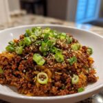 A close-up of a hearty serving of Egg Roll in a Bowl topped with fresh green onions and sesame seeds.