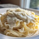 Close-up of fettuccine pasta generously coated in creamy homemade alfredo sauce and topped with grated Parmesan.