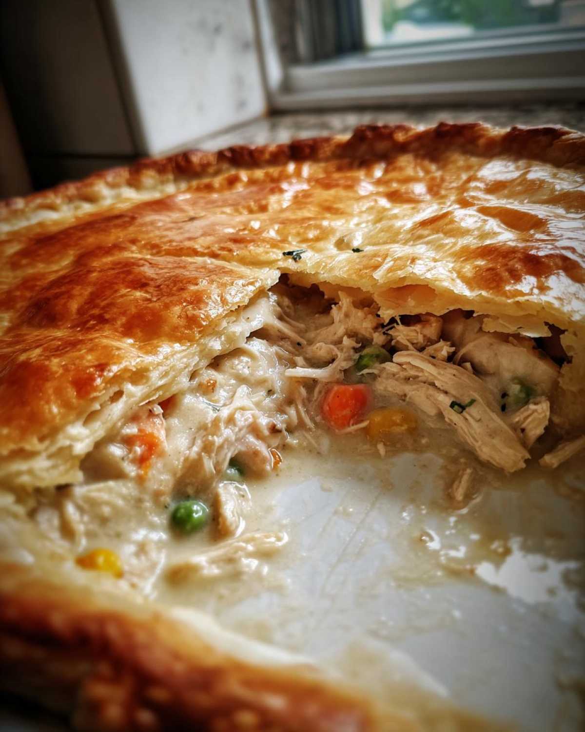 Close-up of a freshly baked turkey pot pie recipe with a piece cut out, revealing creamy filling, shredded turkey, peas, and carrots.
