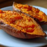 Two halves of perfectly cooked baked sweet potatoes showing bright orange flesh seasoned with pepper.