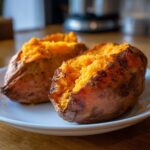 Two perfectly baked sweet potatoes split open showing fluffy, bright orange insides on a white plate.