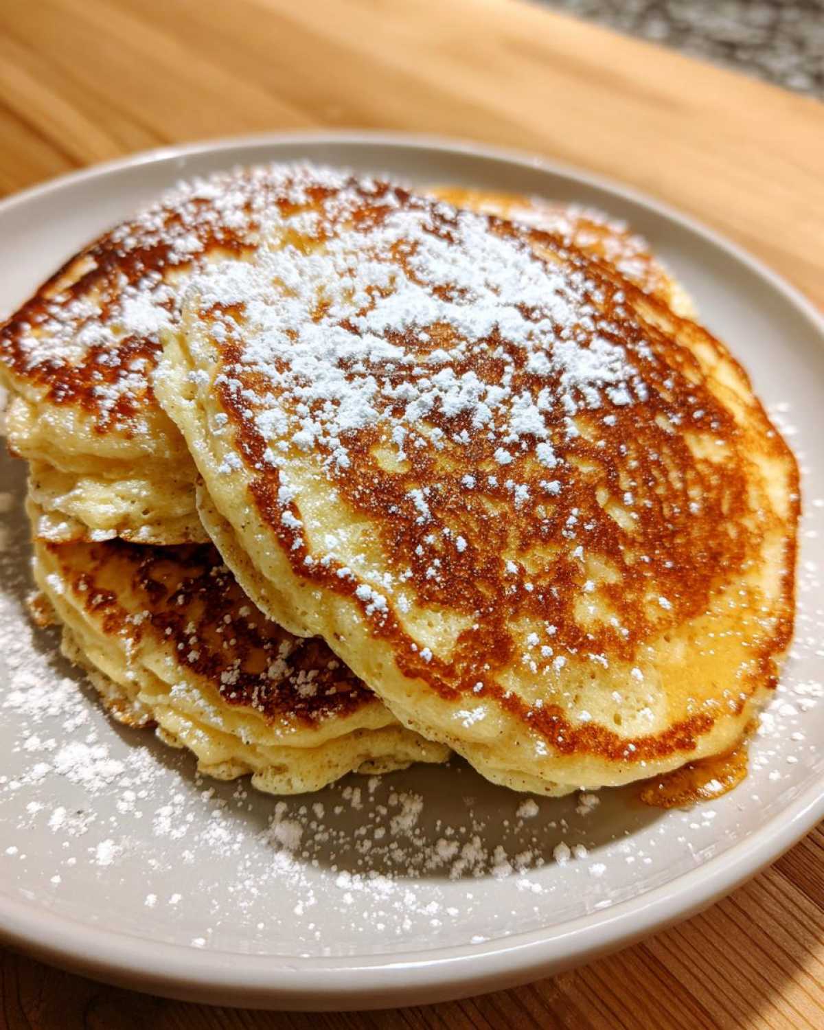 A close-up of a stack of golden brown almond flour pancakes generously dusted with powdered sugar.