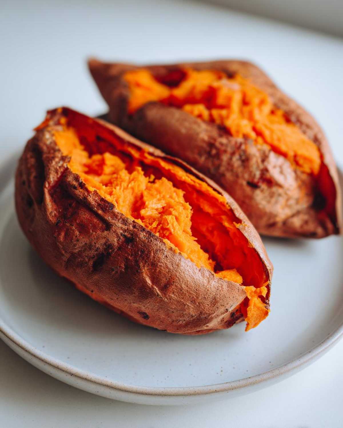 Two fluffy baked sweet potatoes split open, showing bright orange flesh, ready to eat.