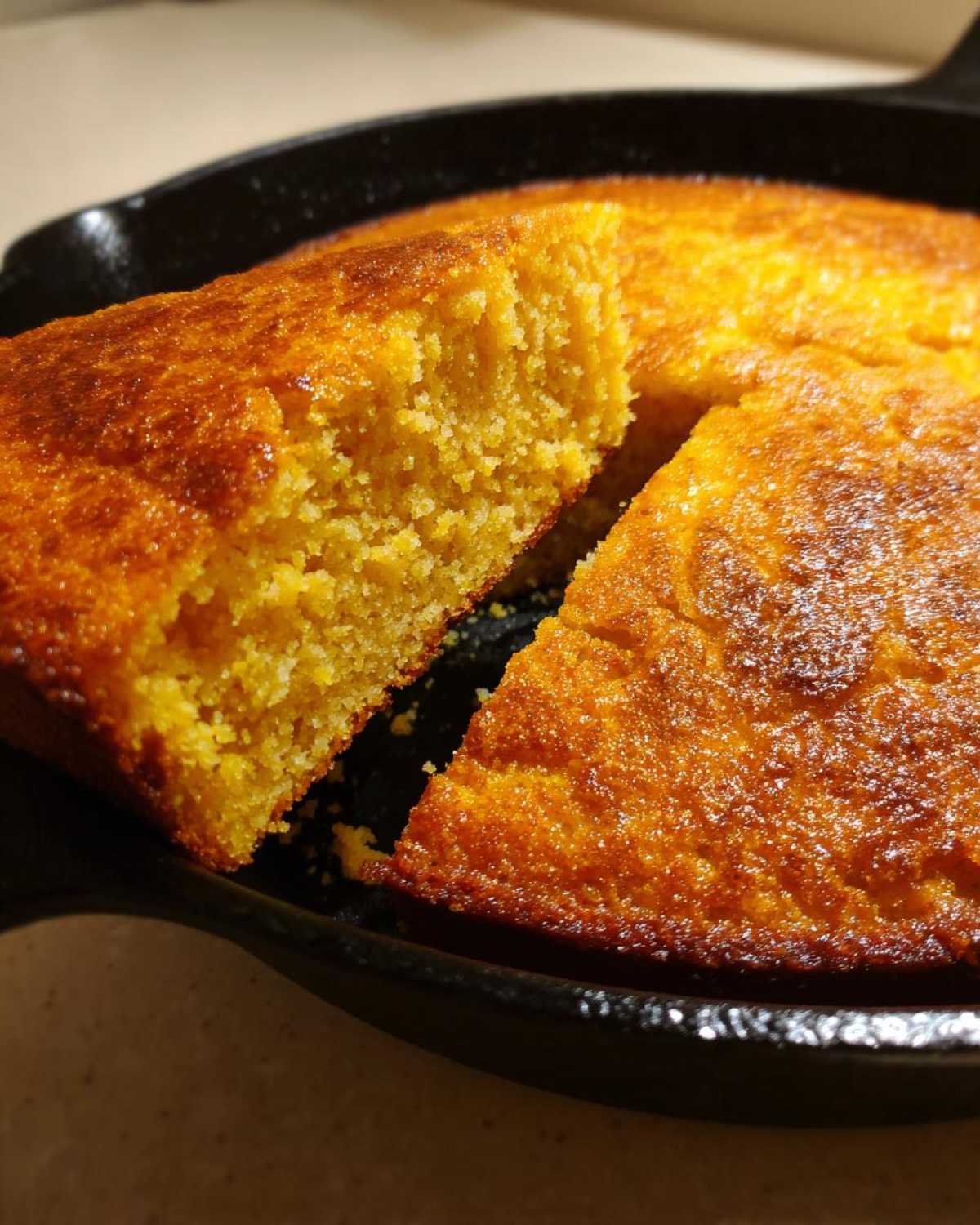 Close-up of fluffy buttermilk cornbread with a deep golden crust, cut open in a black cast iron skillet.