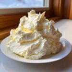 A large, fluffy swirl of homemade cream cheese frosting piled high on a small white plate.