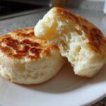 Close-up of a fluffy, toasted english muffin split in half showing its airy interior texture.