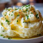 A generous serving of fluffy garlic mashed potatoes drizzled with melted butter and topped with chopped chives.