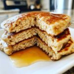 Close-up of a stack of fluffy greek yogurt pancakes cut open, showing the texture and drizzled with maple syrup.
