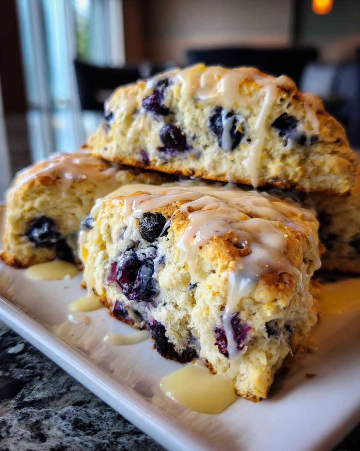 Close-up of fluffy lemon blueberry scones stacked and drizzled with a thick lemon glaze.