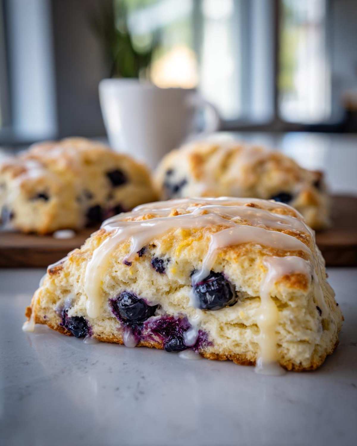 A close-up, cross-section view of a fluffy lemon blueberry scone topped with a thick white glaze, showing juicy blueberries inside.