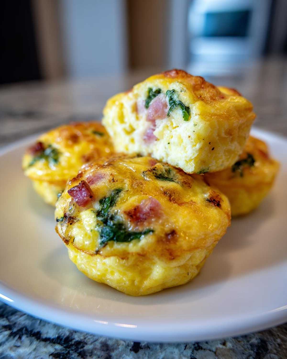 Close-up of fluffy muffin tin egg bites with visible ham and spinach pieces on a white plate.