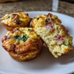 Close-up of fluffy muffin tin egg bites, one cut open showing ham and spinach filling.