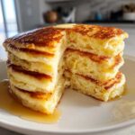Cross-section view of a tall stack of fluffy pancakes topped with melting butter and syrup.