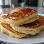 Close-up of a stack of three golden brown, very fluffy pancakes drizzled with syrup.