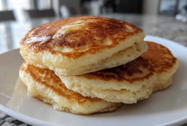 Close-up of a stack of three golden brown, very fluffy pancakes drizzled with syrup.