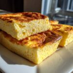 Close-up of fluffy, golden-brown slices of sheet pan eggs stacked on a white rectangular plate.