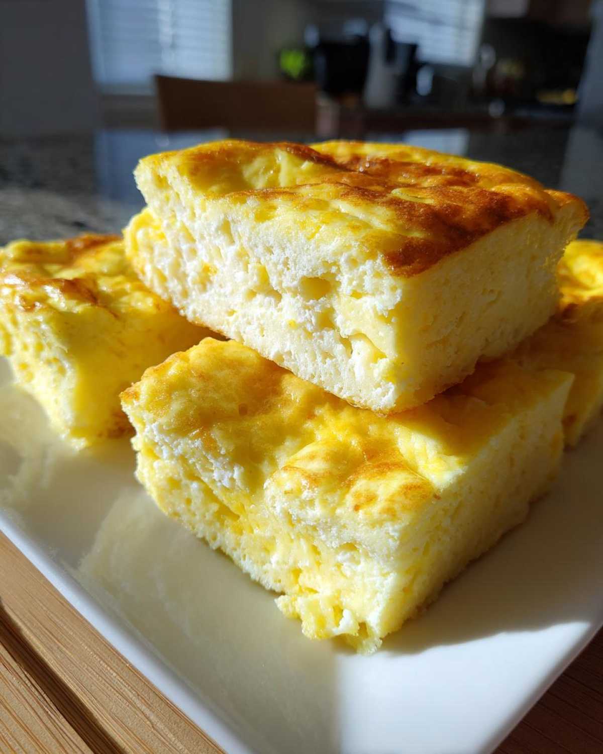 Close-up of fluffy, golden-brown squares of sheet pan eggs stacked on a white plate.