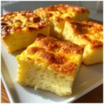 Close-up of fluffy, golden-brown squares of sheet pan eggs served on a white plate.