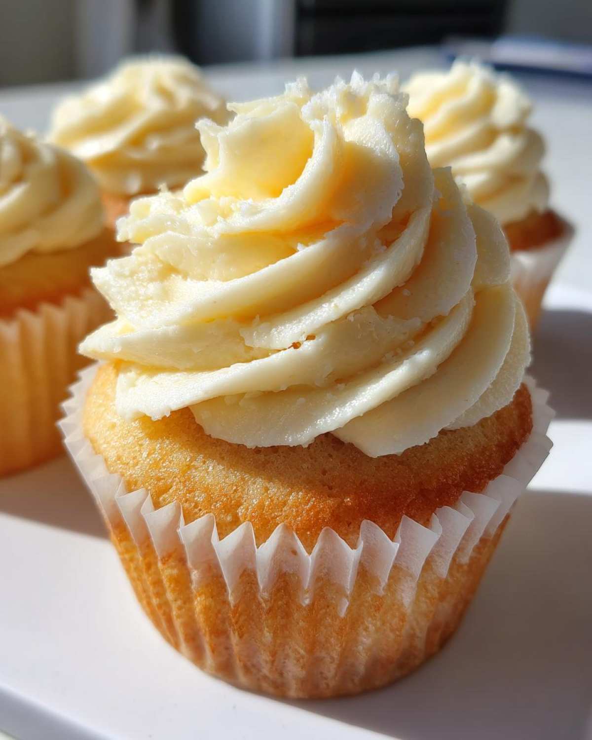 Close-up of a moist vanilla cupcake topped with a swirl of creamy white vanilla frosting.