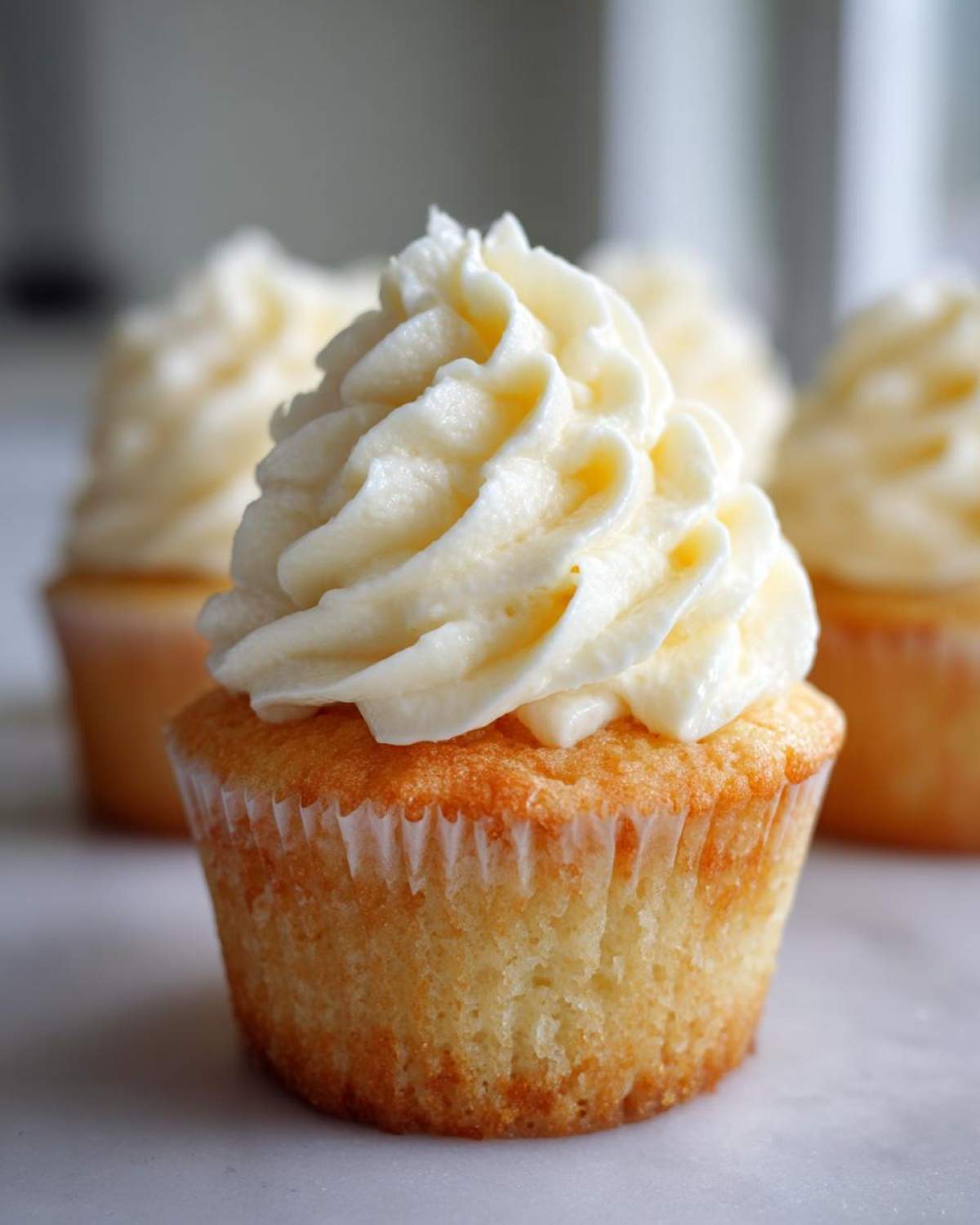 Close-up of a moist vanilla cupcake topped with a tall swirl of white vanilla buttercream frosting.