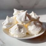 A pile of freshly baked, crisp white meringue cookies with distinct peaks served on a small white plate.