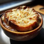Close-up of a bowl of French onion soup recipe topped with a thick, melted, and browned cheese layer over toasted bread.
