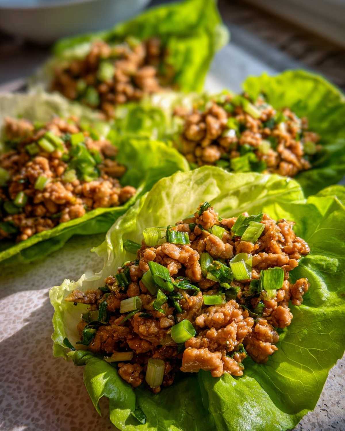 Close-up of savory ground chicken filling topped with green onions served in crisp lettuce cups for chicken lettuce wraps.
