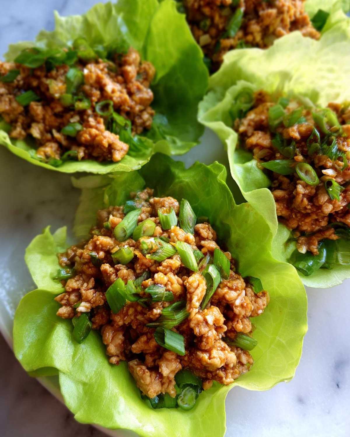 Three servings of flavorful chicken lettuce wraps, filled with ground meat mixture and topped generously with chopped green onions.