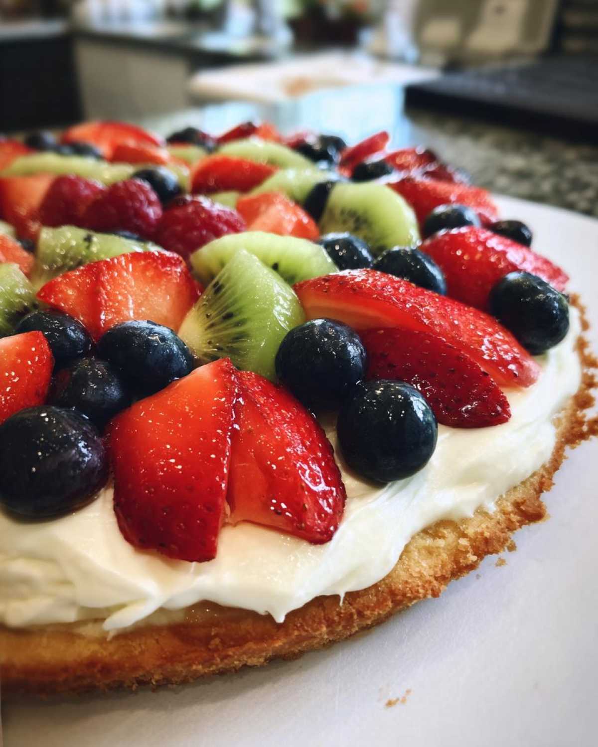 Close-up of a fruit pizza sugar cookie base topped with thick cream cheese frosting and fresh strawberries, blueberries, and kiwi slices.