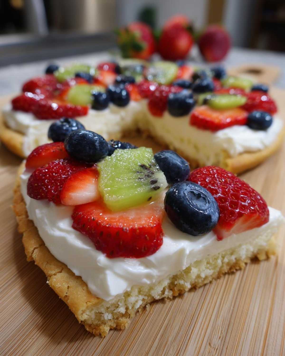 A close-up slice of fruit pizza sugar cookie topped with cream cheese frosting, strawberries, blueberries, and kiwi.