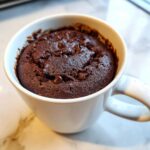 Close-up of a rich, fudgy chocolate mug cake topped with chocolate chips, served hot in a white ceramic mug.