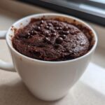 Close-up of a rich, fudgy chocolate mug cake topped with chocolate chips, ready to eat.