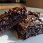Close-up of fudgy sweet potato brownies stacked on a white plate, featuring melted chocolate chips.