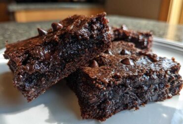 Close-up of fudgy sweet potato brownies stacked on a white plate, featuring melted chocolate chips.
