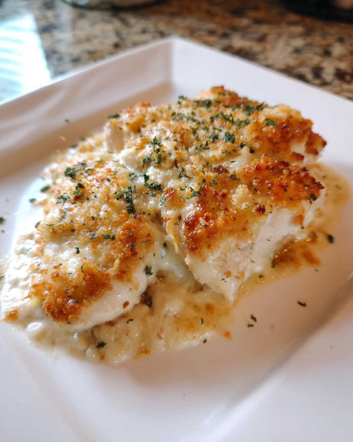 Two pieces of golden-crusted Garlic Parmesan chicken bake smothered in creamy sauce and topped with parsley.