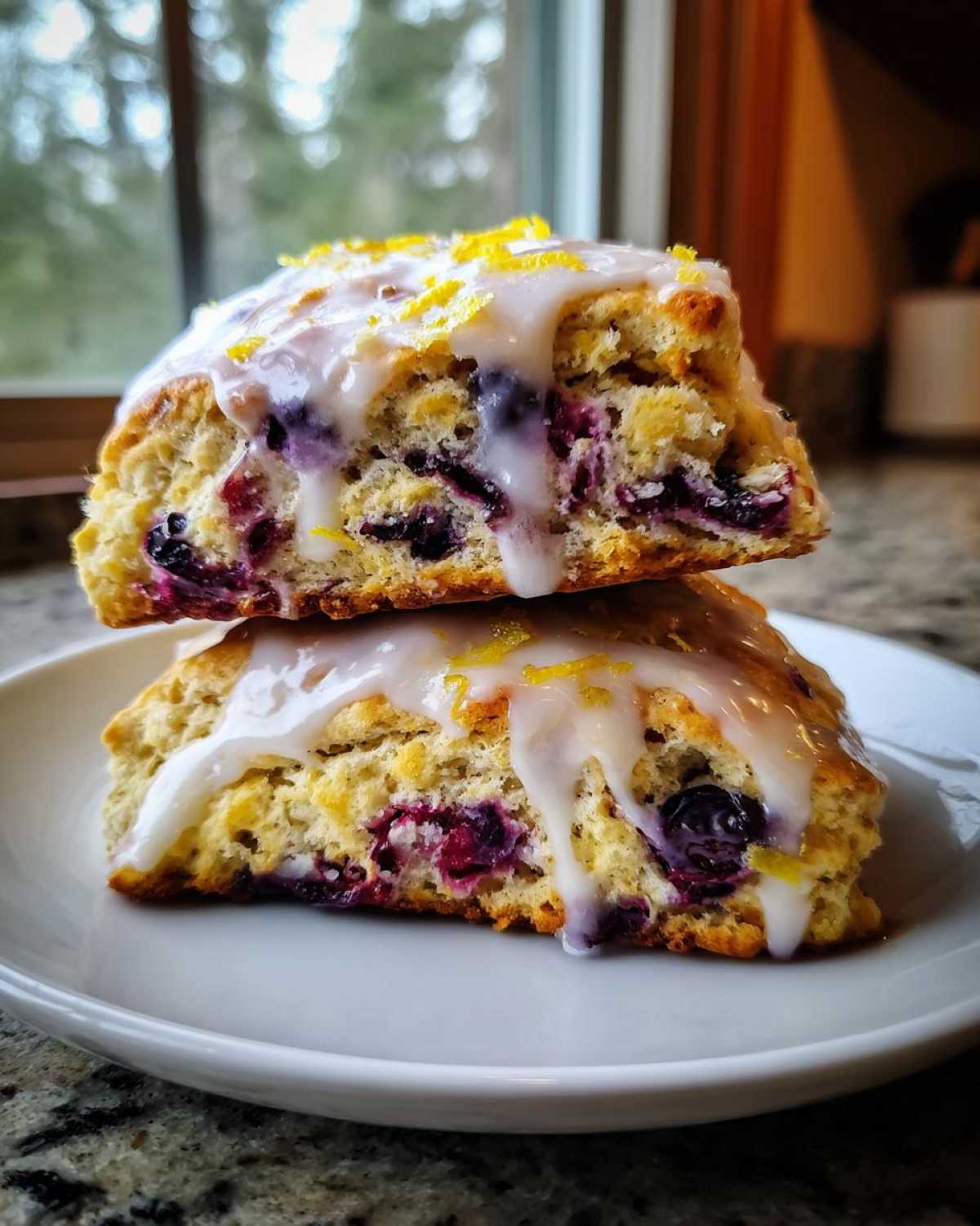 Two delicious blueberry scones stacked, drizzled with lemon glaze and topped with zest.