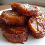 A close-up stack of glistening, caramelized candied sweet potatoes on a white plate.