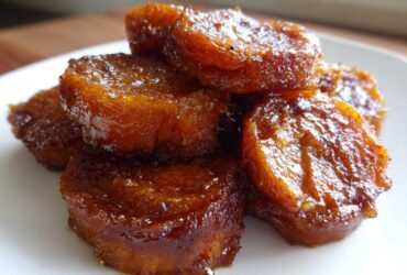 A close-up stack of glistening, caramelized candied sweet potatoes on a white plate.