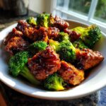 Close-up of saucy, glazed chicken and bright green broccoli florets served in a white bowl.
