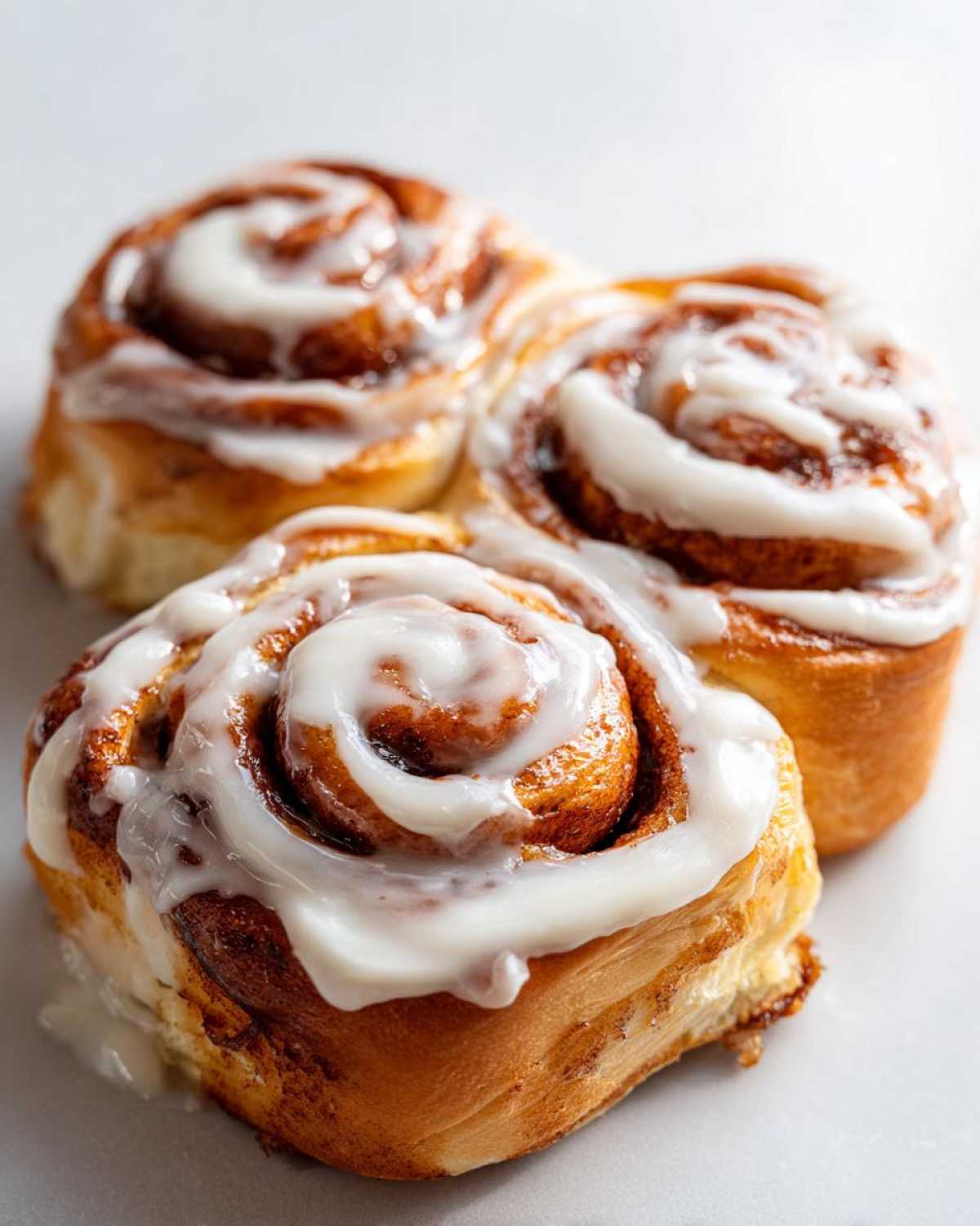 Three freshly baked cinnamon roll pastries covered in thick white icing, ready to eat.