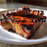 Close-up of a thick, caramelized, and glazed pork steak recipe piece on a white plate.
